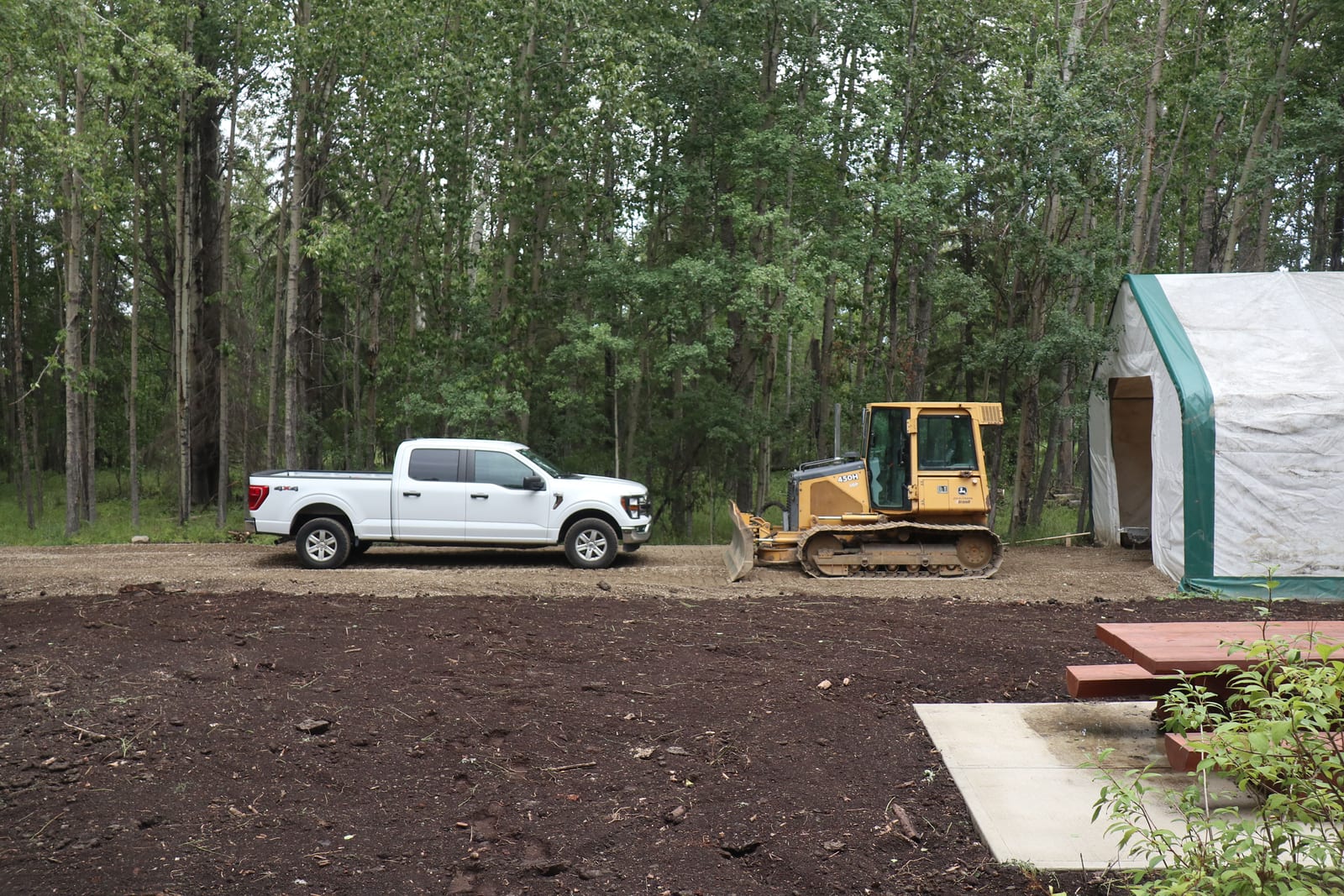 A cleared pad with a company pickup and a dozer parked at the tree line.